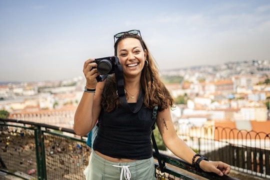 Maria holding her camera with a city view behind her